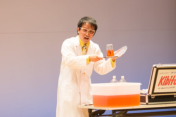 白衣を着たキビートが茶色い液体がコップで科学実験を行う様子